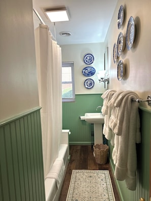 A bathroom with a shower, a sink, and a toilet. There are towels hanging on the wall and a basket on the floor. - A charming bungalow with a Southern feel that’s an quick walk to downtown. (Lewisburg)