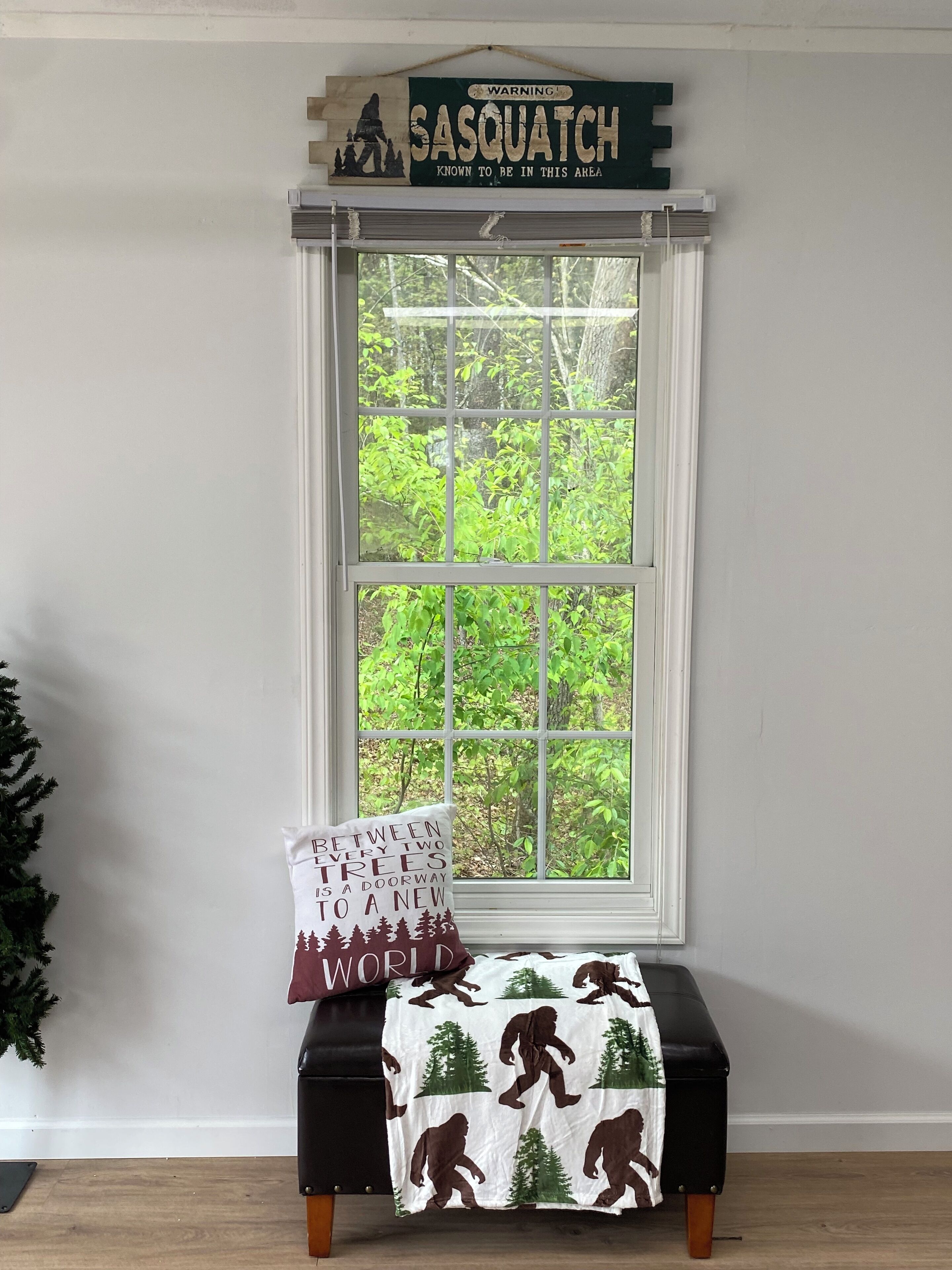 A window with a view of greenery, a warning sign above, a bench with a cushion, and a wall-mounted sign.