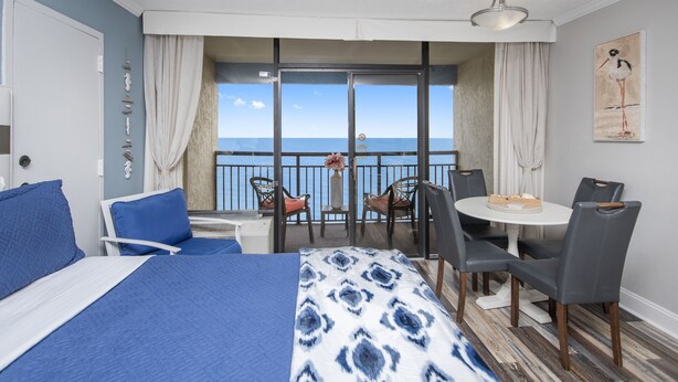 Een hotelkamer met een groot bed, een balkon met tafel en stoelen, en uitzicht op zee.