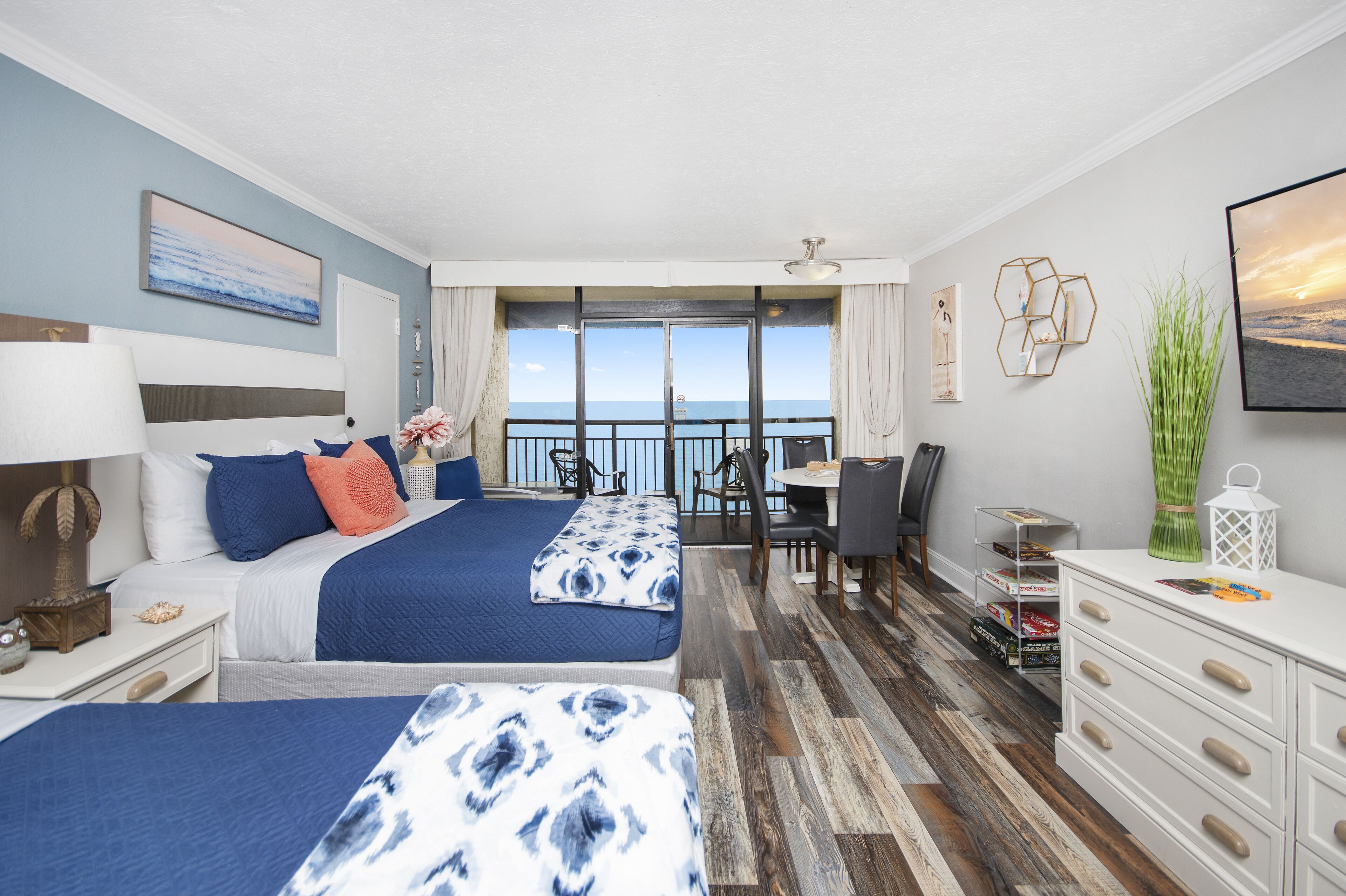 Habitación de hotel con dos camas, zona de comedor, escritorio y vista al mar.