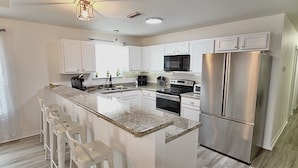 A modern kitchen with white cabinets, stainless steel appliances, a granite countertop, and bar stools. - Peaceful 3-2 Home w/ Pool, 4min to beach, RV P-king, BBQ, Firepit, Fast Internet (Gulf Breeze)