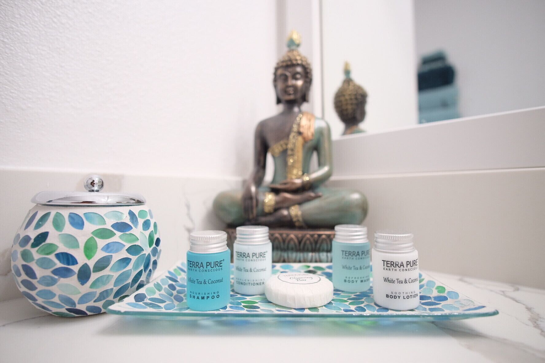 Ein Badezimmer-Waschtisch mit Buddha-Statue, einer Dekoschale und Körperpflegeprodukten von Terra Pure.