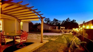 A covered patio with a table and chairs, a fenced backyard, and string lights. - Peaceful 3-2 Home w/ Pool, 4min to beach, RV P-king, BBQ, Firepit, Fast Internet (Gulf Breeze)