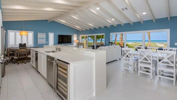 Une cuisine moderne avec des meubles blancs, un grand îlot central et une vue sur la plage.