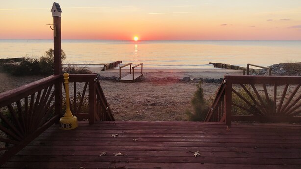 Une terrasse en bois qui mène à une plage, avec un coucher de soleil en arrière-plan.