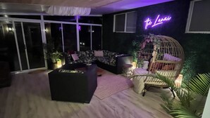 A modern living room with a black sofa, a wooden ceiling, and a neon sign reading "The Lanai".
