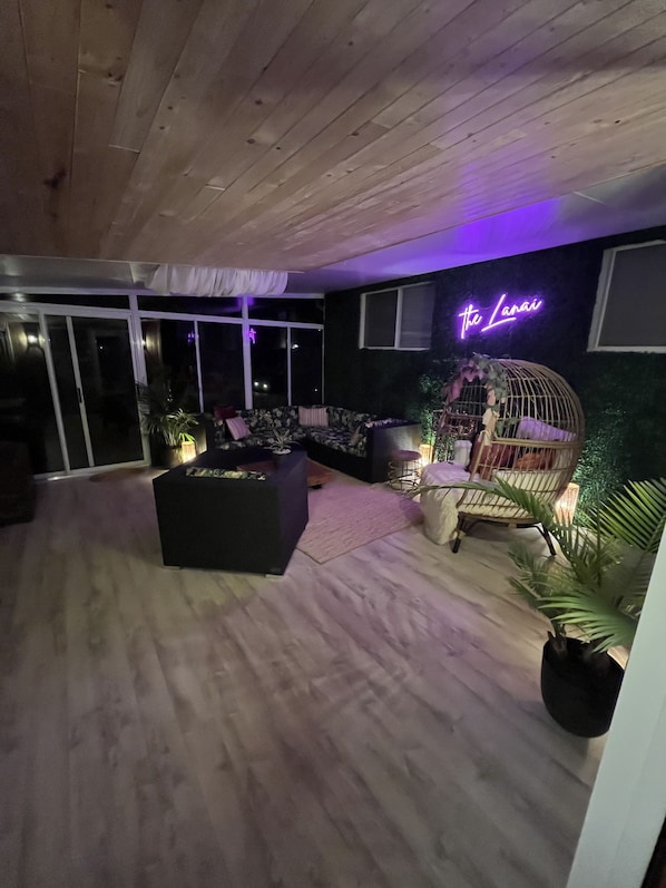 A modern living room with a black sofa, a wooden ceiling, and a neon sign reading "The Lanai". - Private Beach! Year Round Secluded Forest Retreat in Port Franks. Hot Tub! (Port Franks)