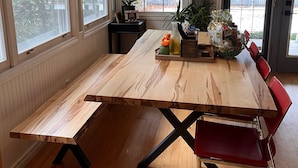A dining area with a wooden table, red chairs, a hanging light fixture, and large windows.