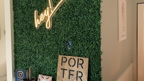 A reception desk with a green wall backdrop, a neon 'hey!' sign, a wooden sign reading 'PORT FRANKS', and a potted plant.