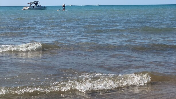 A beach with calm waters, a boat, and a person paddleboarding.