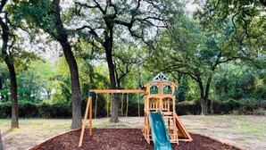 A playground with a slide and swings, surrounded by trees.