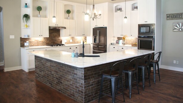 A spacious kitchen with white cabinetry, a large island, and a brick accent wall.