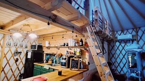 Un intérieur chaleureux et rustique, avec une table à manger en bois, des tabourets de bar, un coin cuisine et un escalier en colimaçon menant à un étage supérieur.