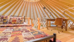 Une yourte avec un plafond arrondi, un lit recouvert d’une couverture à motifs, un bureau et une chaise.