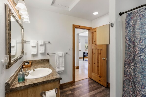 A bathroom with a wooden vanity, a large mirror, and a shower curtain with a paisley pattern.