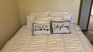 Ein ordentlich bezogenes Bett mit weißer gesteppter Tagesdecke und zwei dekorativen Kissen mit Aufschrift.