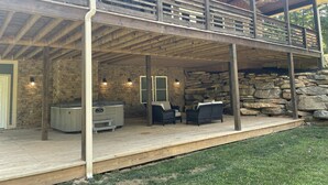 A covered outdoor area with stone walls, wooden deck, and outdoor furniture. - New 4k sf Mdrn Farmhouse-hot tub-fire pit-games on 3 acres 7 minutes from dwntn. (Asheville)