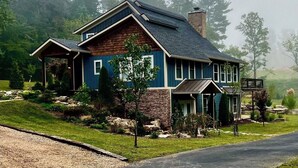 A two-story house with a stone foundation, blue siding, and a dark roof. - New 4k sf Mdrn Farmhouse-hot tub-fire pit-games on 3 acres 7 minutes from dwntn. (Asheville)