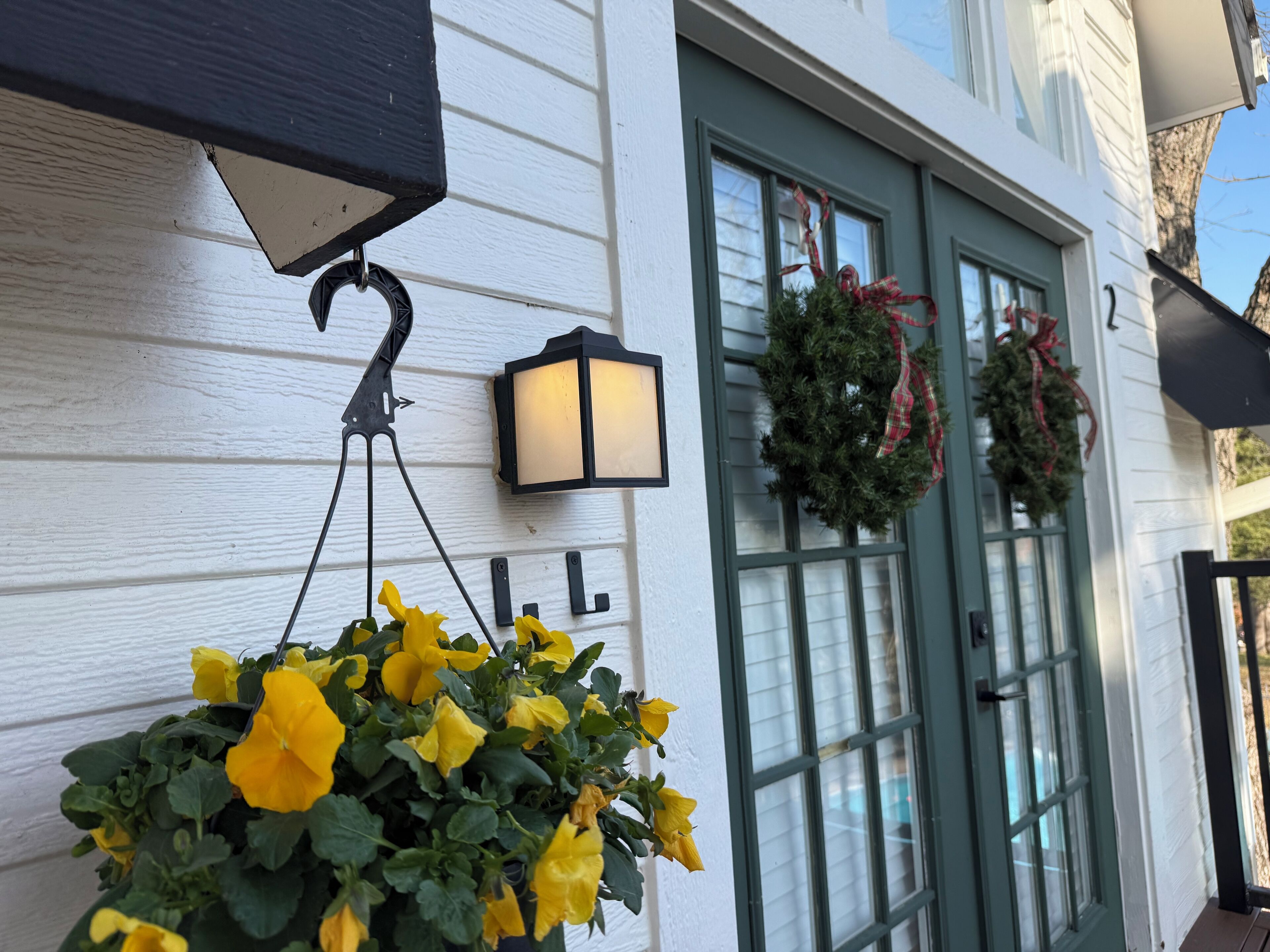 En vit byggnad med en grön dörr, en hängande lampa och en krans på dörren.