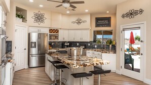 A modern kitchen with white cabinets, stainless steel appliances, a granite countertop, and a ceiling fan. - Luxury Lake View Villa with  Pool, Spa, Sleeps 14, Boat parking (Lake Havasu City)
