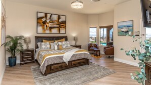 A spacious bedroom with a large bed, a chandelier, a view of the outdoors, and a television. - Luxury Lake View Villa with  Pool, Spa, Sleeps 14, Boat parking (Lake Havasu City)