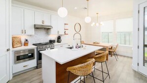 A modern kitchen with white cabinetry, a central island with bar stools, and pendant lighting. - Eastside Oasis *Walk to Bars, Brews & Good Eats* (Austin)