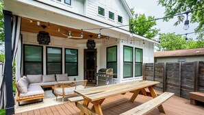 A wooden deck with a picnic table and a sofa, a grill, and string lights. - Eastside Oasis *Walk to Bars, Brews & Good Eats* (Austin)