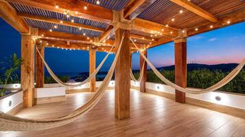 Una terraza de madera al aire libre con una hamaca, luces colgantes y vistas del paisaje.