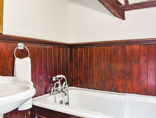 A bathroom with a wooden panel wall, a white bathtub, and a white sink.
