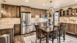 A modern kitchen with wooden cabinets, stainless steel appliances, and a dining area with wooden chairs. - Ski-In Ski-Out, Skiwatch - Peak 8 Breckenridge, Sleeps 12  Newly Renovated (Breckenridge)