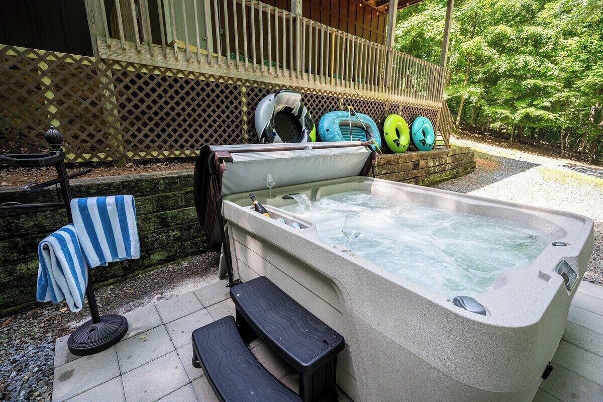 A hot tub with a wooden deck, a bench, and a towel rack. Inflatable rings are visible in the background.