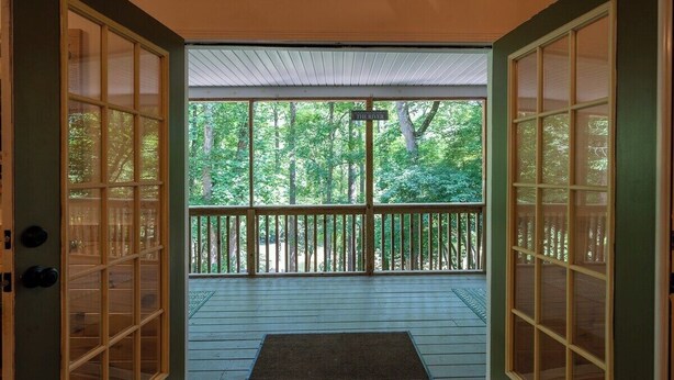 A wooden deck with a railing, a door with glass panels, and a view of a forested area. - Fun Riverside Cabin: Indoor Games+Hot Tub+Firepit (Ellijay)