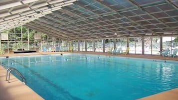 Une piscine intérieure dotée d’un toit en verre, entourée de chaises longues et d’un espace aménagé au bord de la piscine.