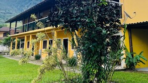 Un edificio amarillo con un porche cubierto y un jardín con rocas y plantas.