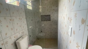 Un baño con inodoro, ducha y una ventana pequeña.
