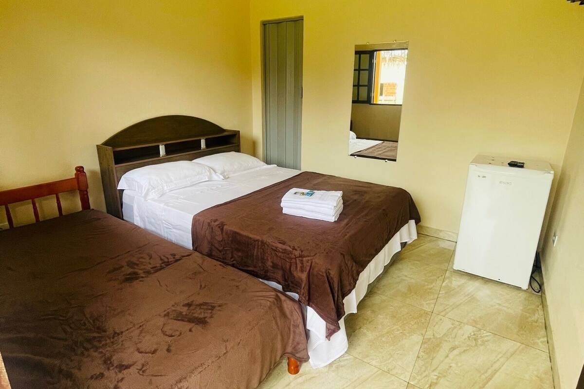 Ein Zimmer mit zwei Betten, einem kleinen Schreibtisch, einem Fenster und einem Kühlschrank.