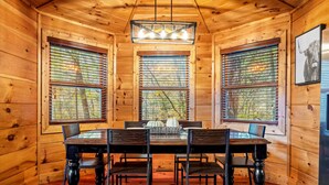 Interior de una cabaña de madera con una mesa de comedor, cuatro sillas y una araña.