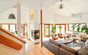 A spacious living area with a wooden staircase, large windows, and a fireplace.