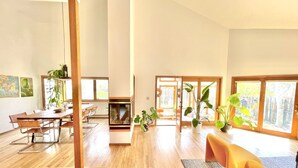 A spacious living area with a wooden floor, a dining table with chairs, a fireplace, and large windows offering views of the outdoors. - Spacious Designer Home in Boulder Perfect for Families and Groups (Boulder)