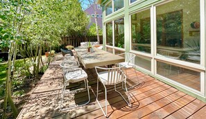 An outdoor patio with a wooden deck, a long table, and white chairs. - Spacious Architect Home Ideal for Families +Groups (Boulder)