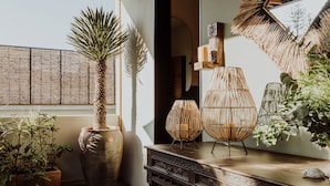 Una habitación con un ventanal grande, una mesa de madera con adornos varios y plantas en macetas.