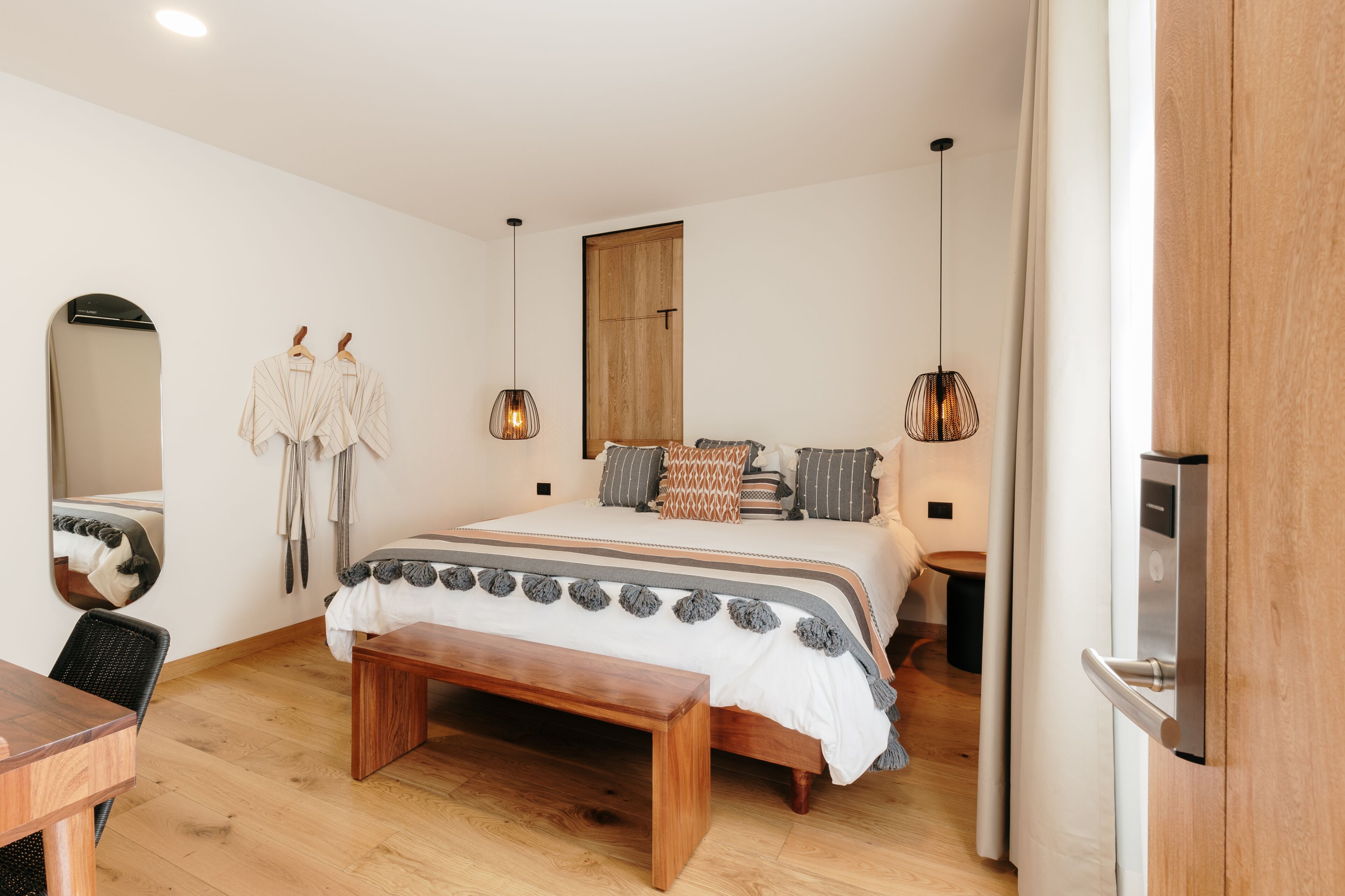 Une chambre avec un lit en bois, un banc, un miroir et des lampes suspendues.