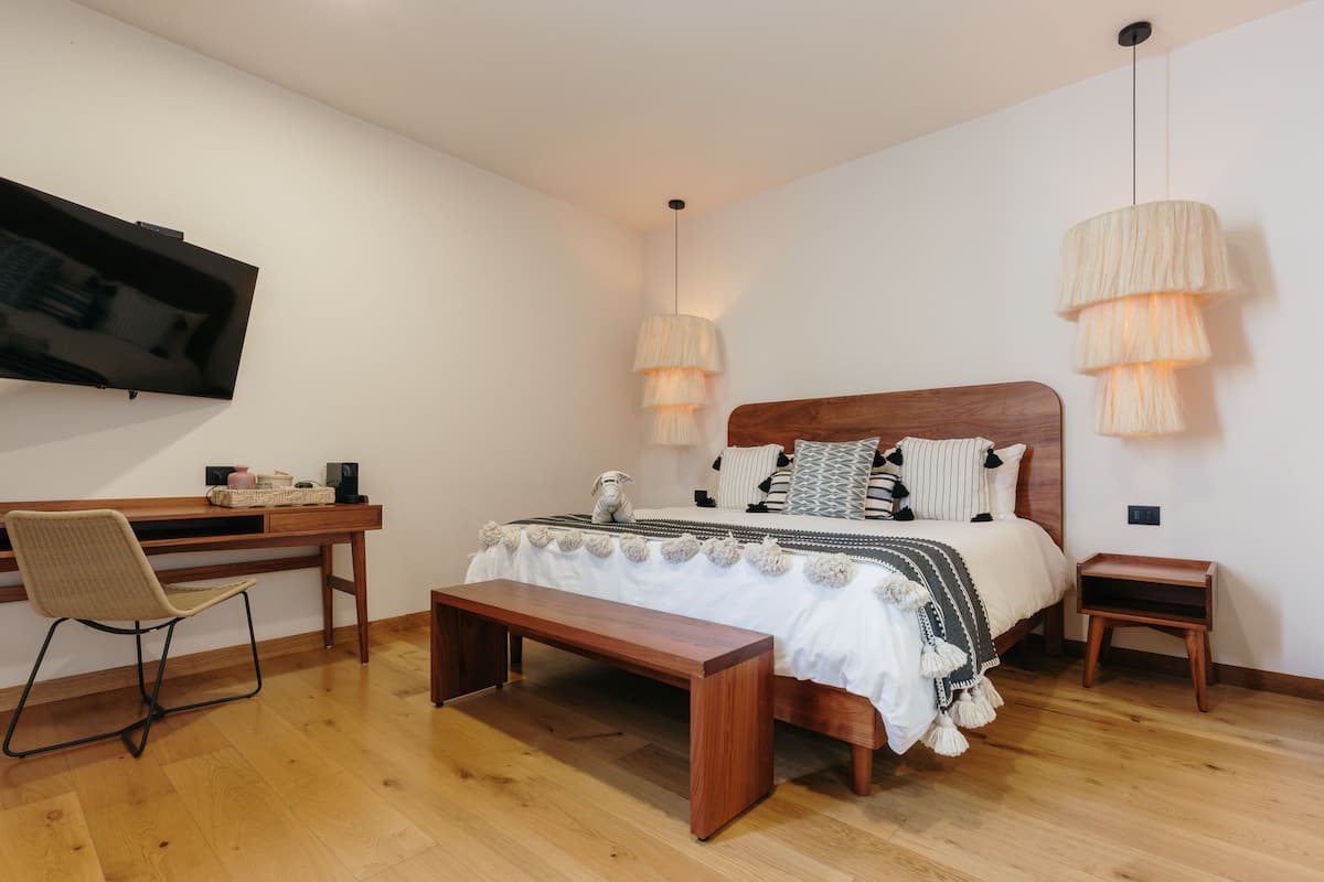 Un dormitorio con una cama de madera, un escritorio, una silla y un televisor montado en la pared.