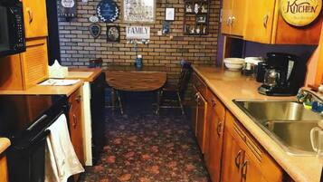 Cuina amb armaris de fusta, paret de maó, cafetera i un rètol que diu "Grandma's Kitchen".