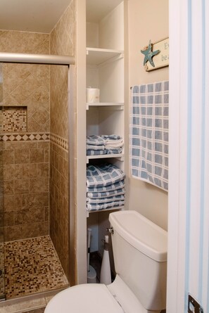 Une salle de bain avec une douche, des toilettes et des étagères où sont pliées les serviettes.