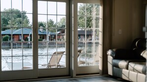 A room with a large sliding glass door leading to a dock area with boats and a view of houses across the water. - River & Bay Views! Shirley’s Temple! BAY CITY, MI (Bay City)