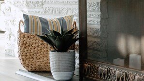 A fireplace with a textured white brick wall, a woven basket with a plant, and a striped pillow. - River & Bay Views! Shirley’s Temple! BAY CITY, MI (Bay City)
