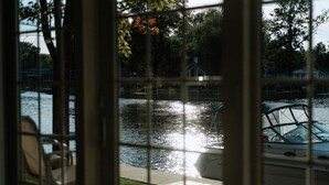 A view through a window with a metal grid, overlooking a body of water with boats, a dock, and a house in the background. - River & Bay Views! Shirley’s Temple! BAY CITY, MI (Bay City)