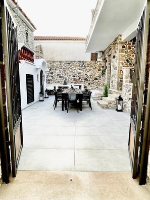 A courtyard with a stone wall, a dining table, and chairs. - Trocadero Luxury Suites (Ermionida)