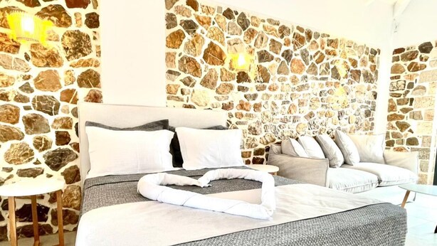 Ein Schlafzimmer mit einer Steinwand, einem Bett mit grauer Bettwäsche, einem Sofa und einem kleinen Tisch.